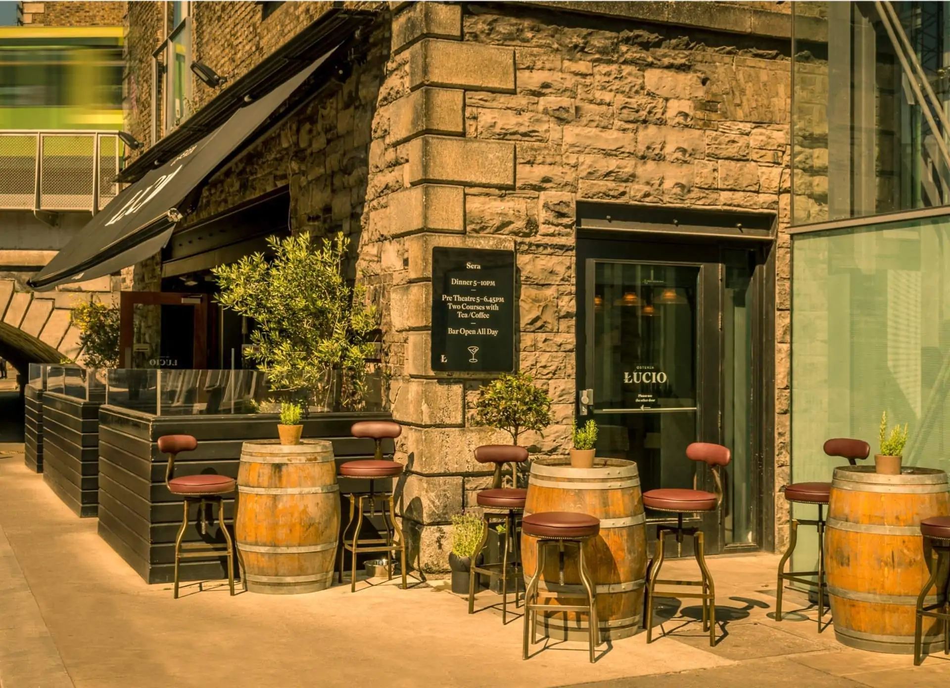 Outdoor seating at Osteria Lucio in Grand Canal Dock in Dublin consists of wine barrel tables, red leather high chairs, plus a covered enclosed seating area.