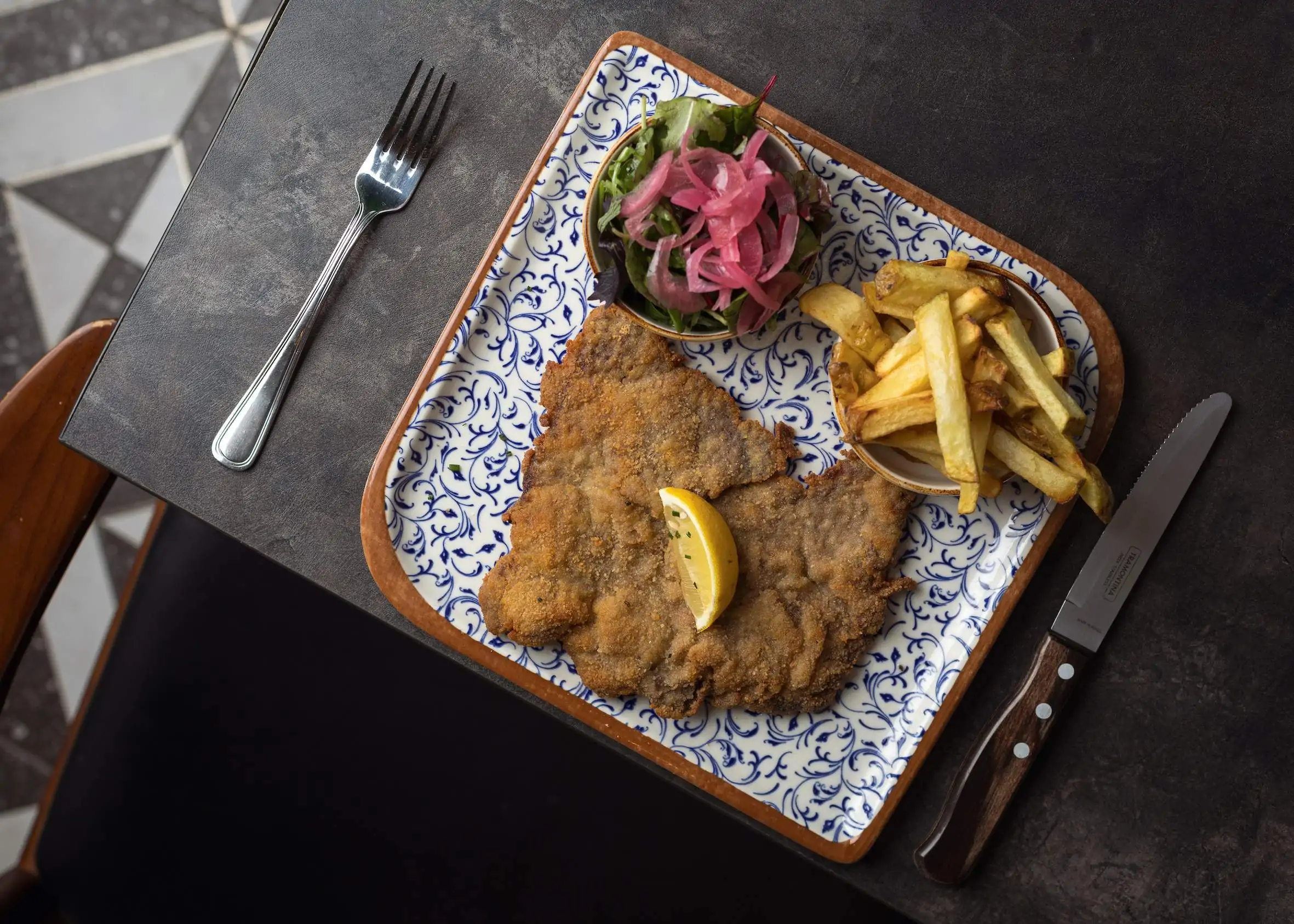 A breaded cutlet of chicken on a patterned plate is served with chips and salad at Peperina City Bistro, a restaurant in Dublin