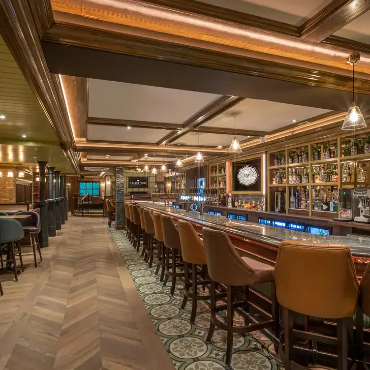 The long bar at The Black Forge, lined with cushioned, tall chairs on top of patterned flooring.