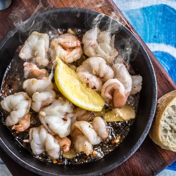 A bowl of seafood served with a lemon wedge, bubbling and steaming hot.