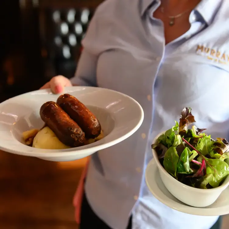 A waitress carries a dish of sausages and mashed potato in one hand and a bowl of salad in the other at Murray’s Bar, one of the best pubs in Dublin.