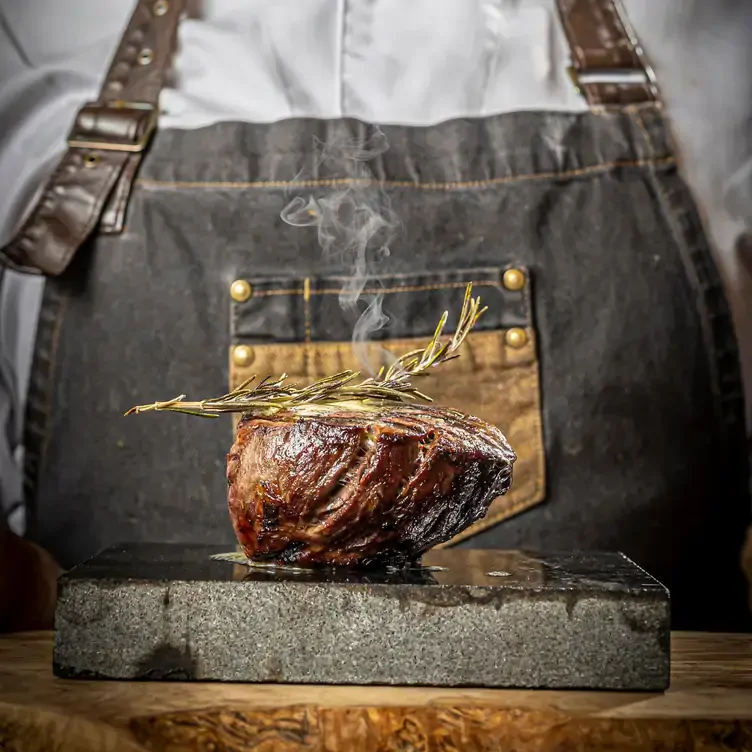 Someone with an apron stands behind a chunk of steak on a stone slab topped with a sprig of rosemary at The Black Forge, one of the best pubs in Dublin.