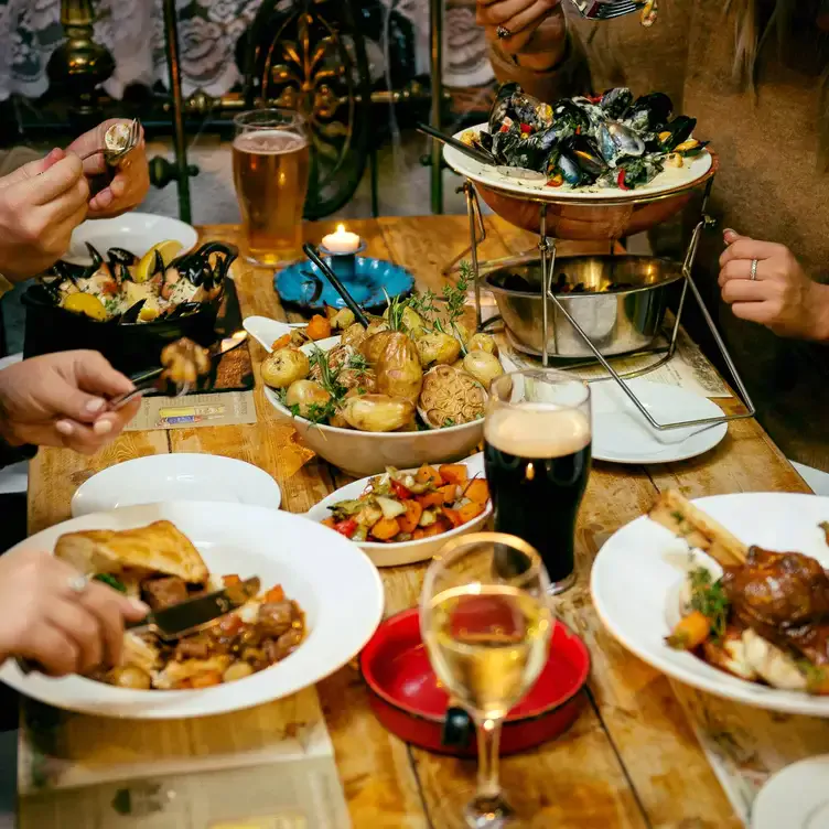 Diners sit around a wooden table eating dishes of lamb, mussels and potatoes.