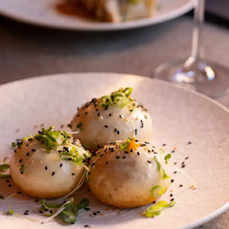 Three Chinese dumplings topped with black sesame and herbs sit on a white bowl and Nan Chinese, a restaurant in Dublin.