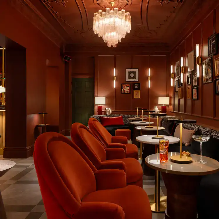 Interior view of Pen & Player, one of the best cocktail bars in Dublin, showing comfortable red velvet seats across from bench seating, with cocktails on the tables.