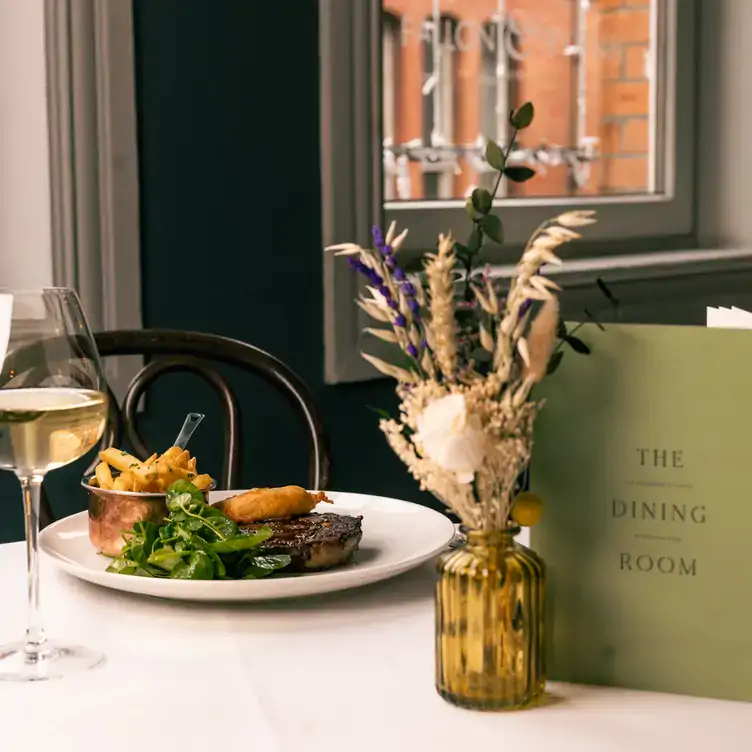 A plate of steak with sides and a glass of white wine on a white tablecloth at Fallon & Byrne, one of the best affordable restaurants in Dublin.